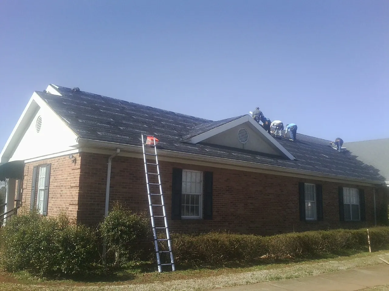 Crew tearing shingles off a brick ranch roof with a ladder set — Metal Roof Repair work by our crew in Allport