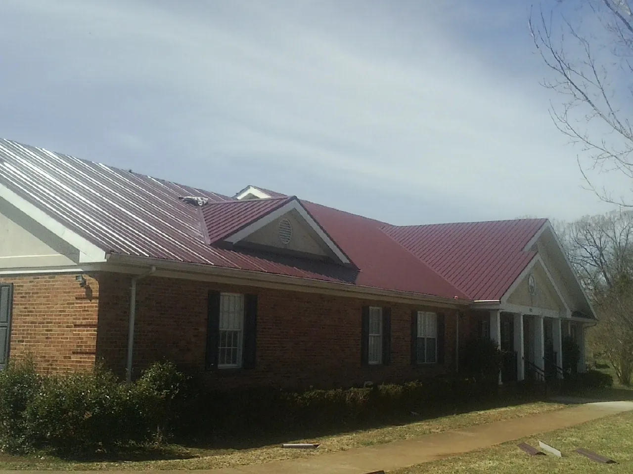 Red metal roof with gabled entries on a long brick building, from a Hail Damage Roof Repair job in Allport