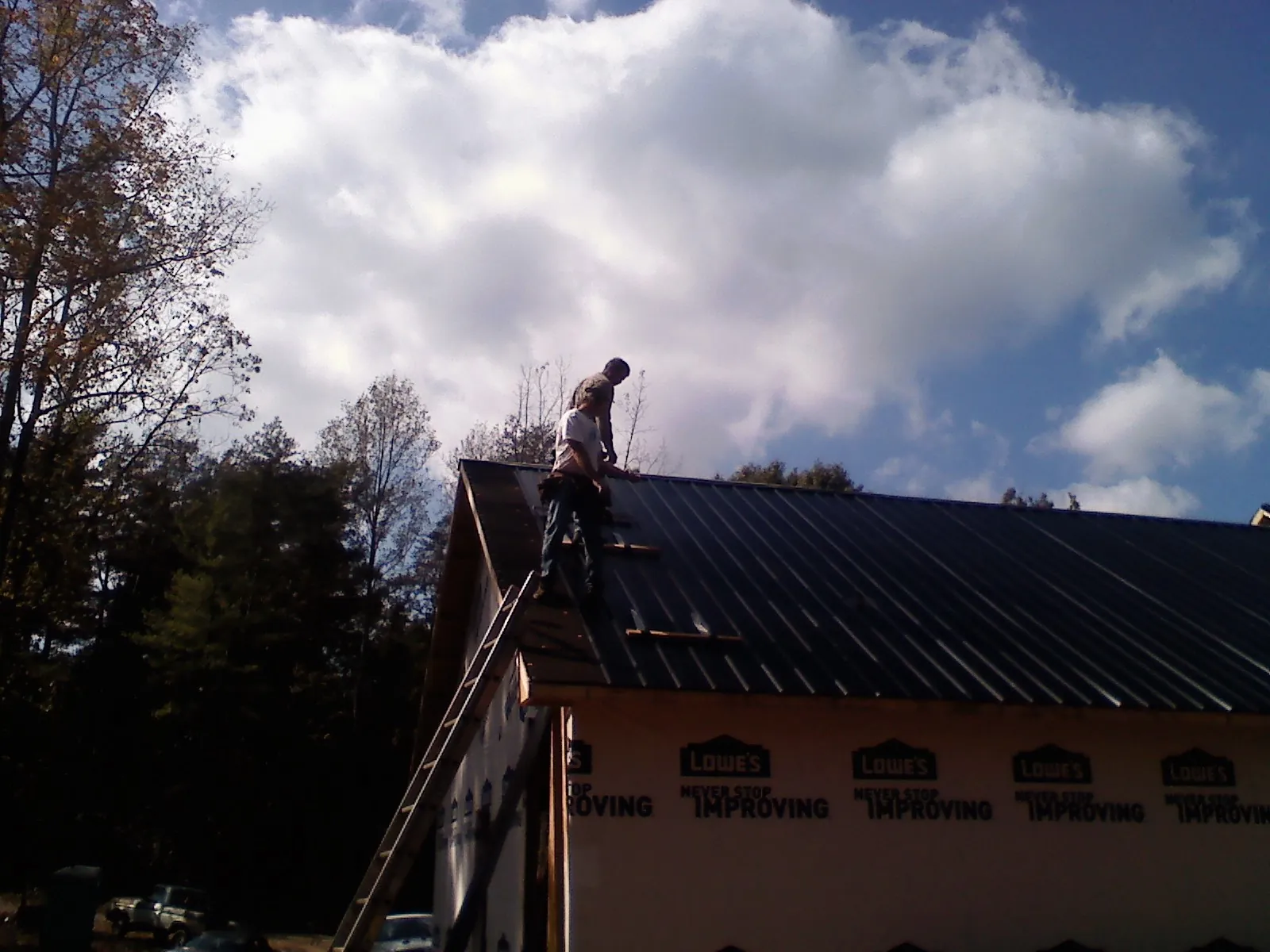 Roofer fastening dark metal panels high against a cloudy sky in Allport