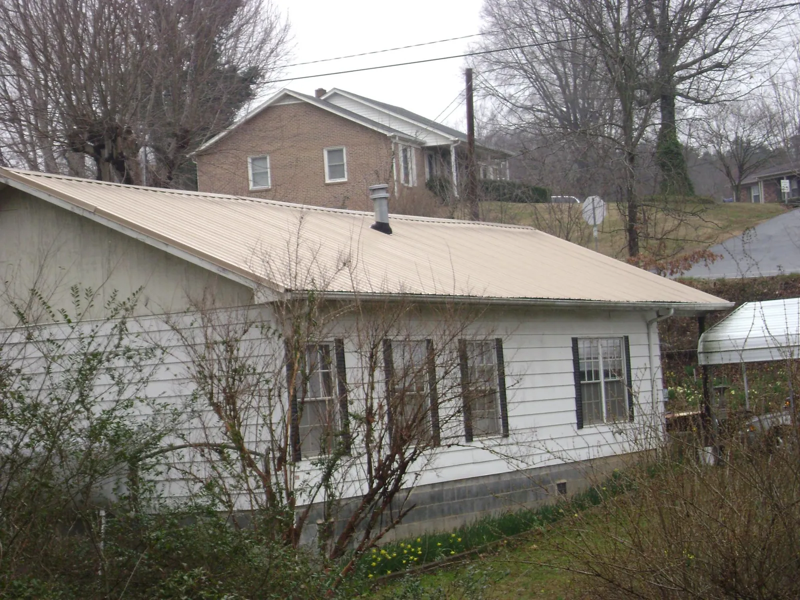 Tan metal roof on a white sided house set into a hillside — Commercial Roofing by Roofing Brothers in Allport